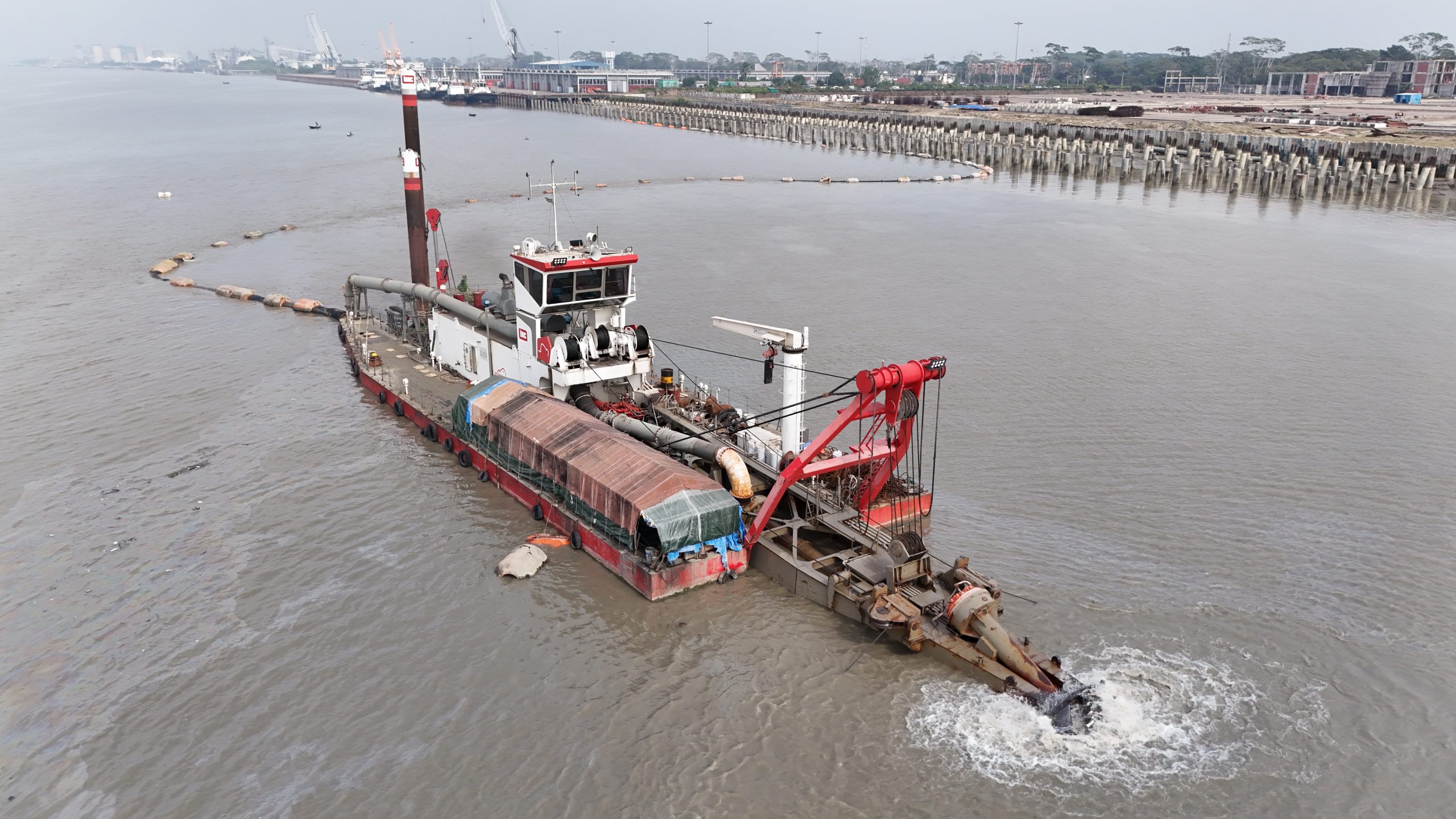 Dredger operating close to a jetty, removing underwater debris for safe vessel docking.