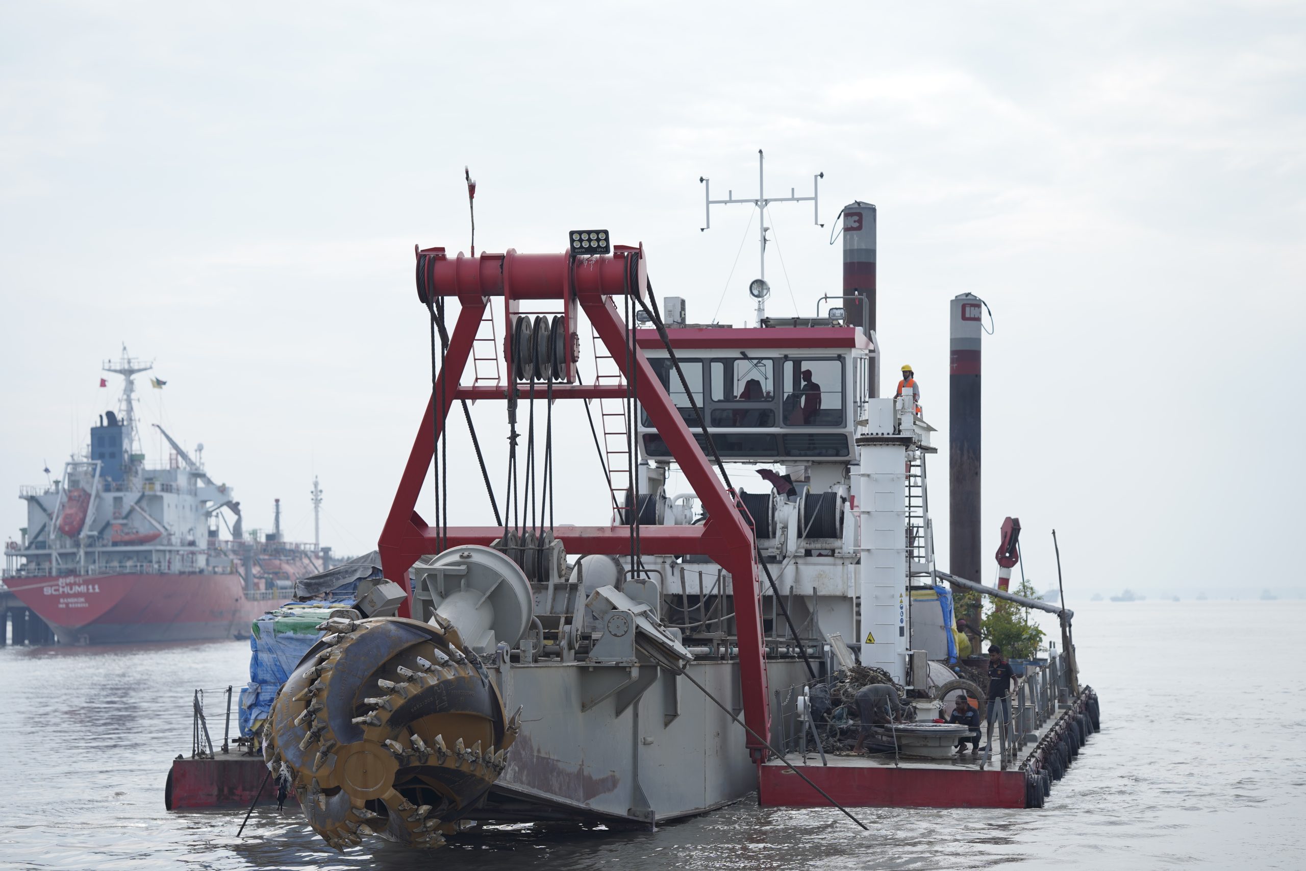 Dredging vessel in action, clearing sediment from a busy shipping channel near the coast.