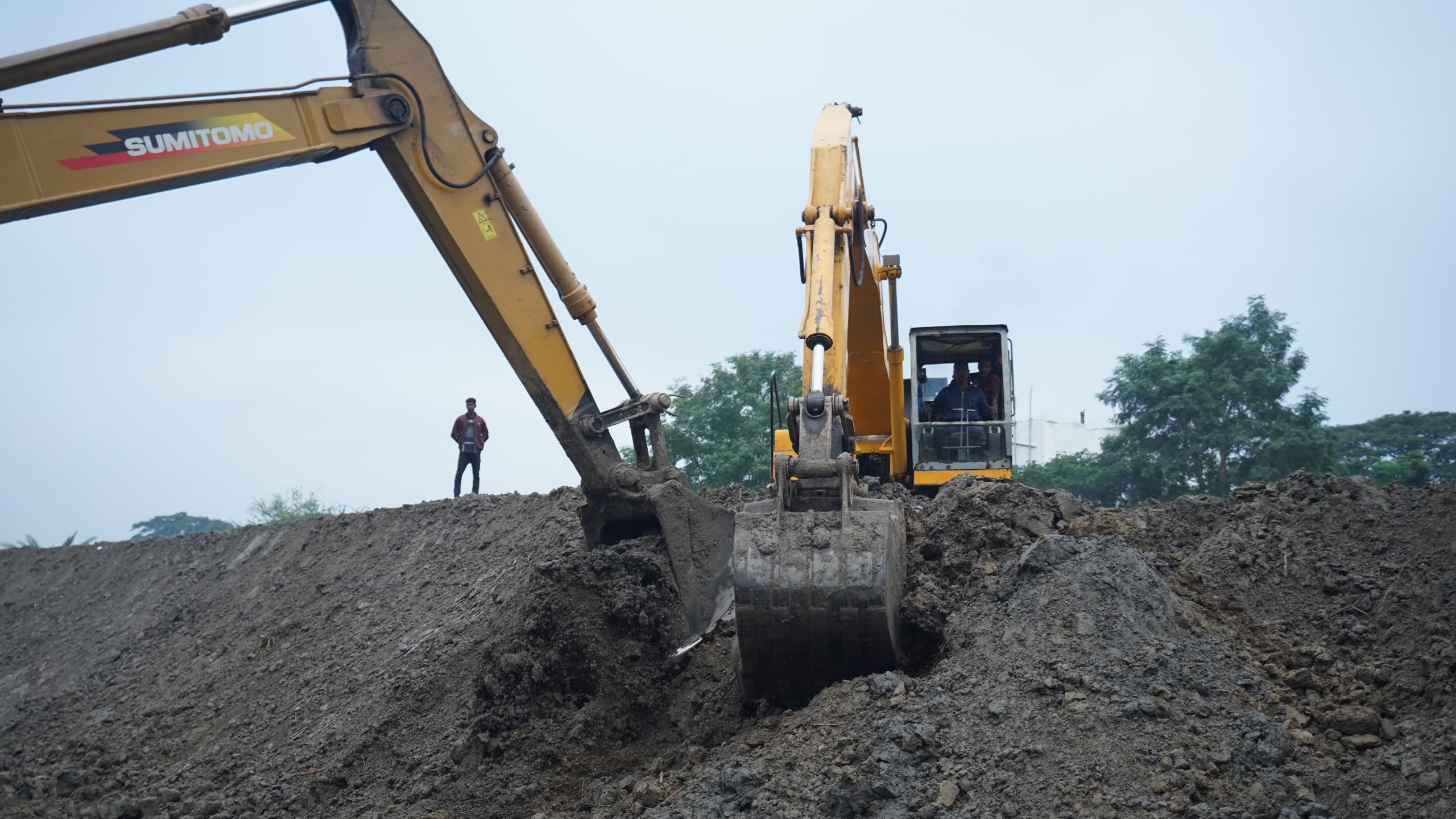 Excavator working beside the river to reinforce a sand-based dyke structure.